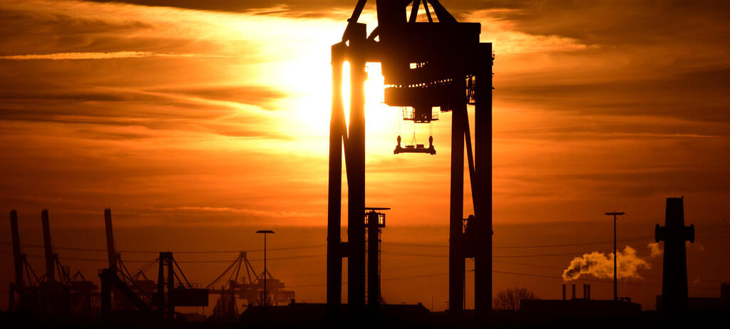 Hamburg: Die Sonne geht hinter Containerbrücken im Hafen unter.
