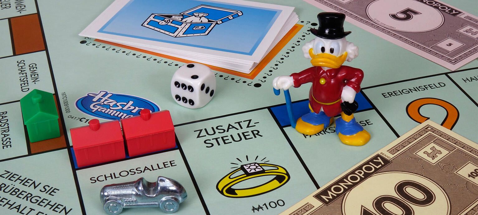 Auf einem Monopolyspiel befindet sich Spielgeld und eine Figur von Dagobert Duck. Vermögensteuer