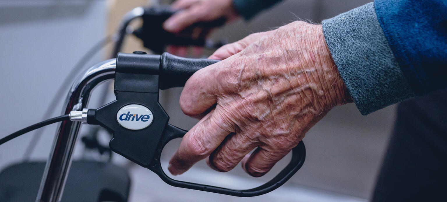 die faltige Hand eines über 90-jährigen Mann umgreift den Griff eines Rollators