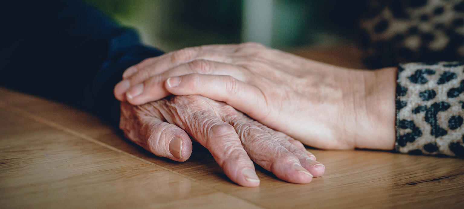 eine Hand liegt auf einer Hand einer alten Frau