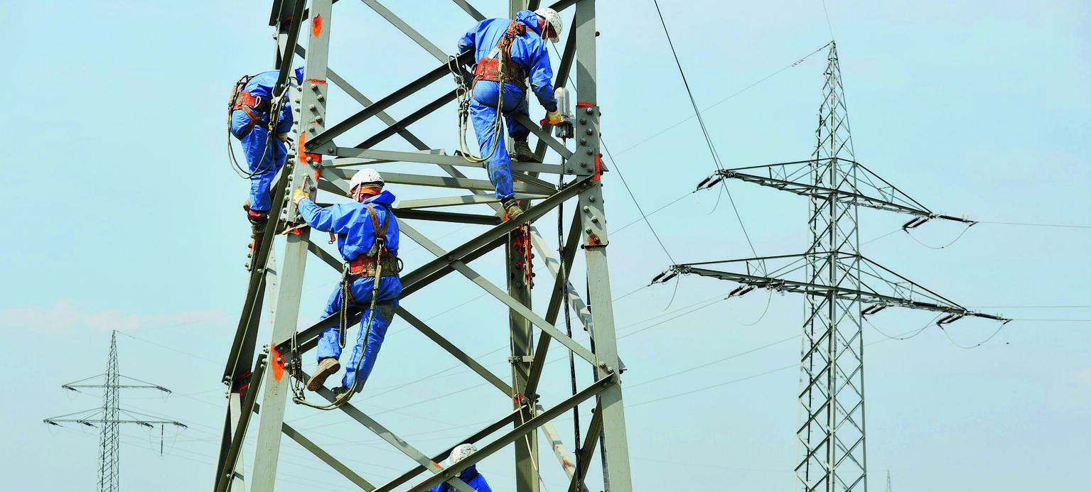 Polnische Arbeiter sind dabei, den Rostschutz an einem Strommast zu erneuern.