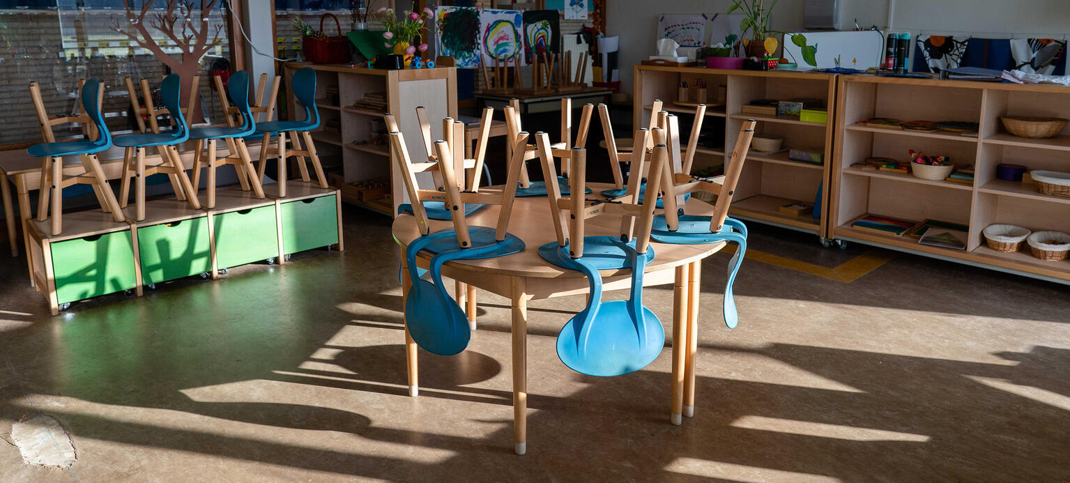 Ein leerer Raum zur Kinderbetreuung. Darin stehen Tische auf denen bunte Stühle hochgestellt sind.