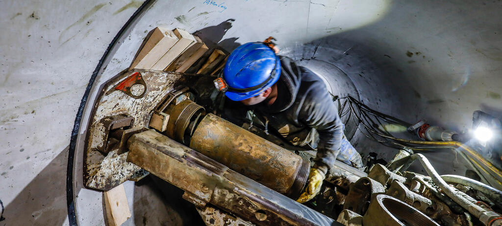 Ein Mann mit Helm und Arbeitskleidung arbeitet in einem Kanal um eine Hausanschlussbohrung durchzuführen. 
