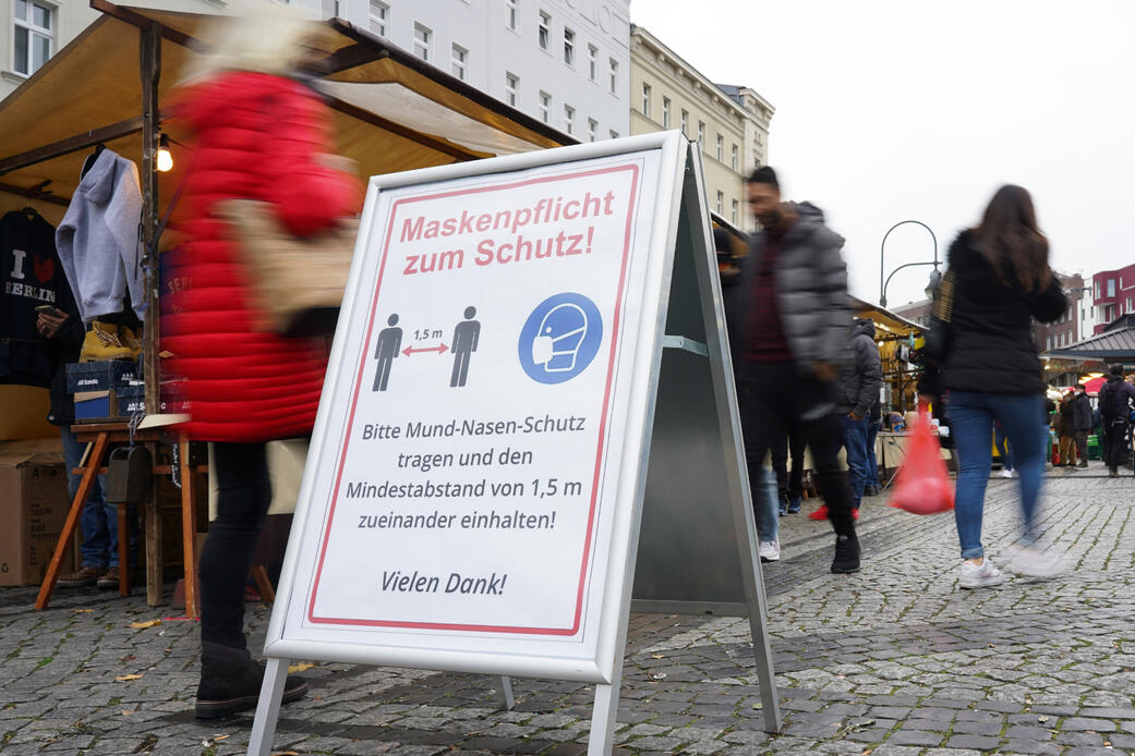 Ein Schild, das auf die Maskenpflicht und das Abstandsgebot hinweist, steht auf dem Wochenmarkt auf dem Hermannplatz