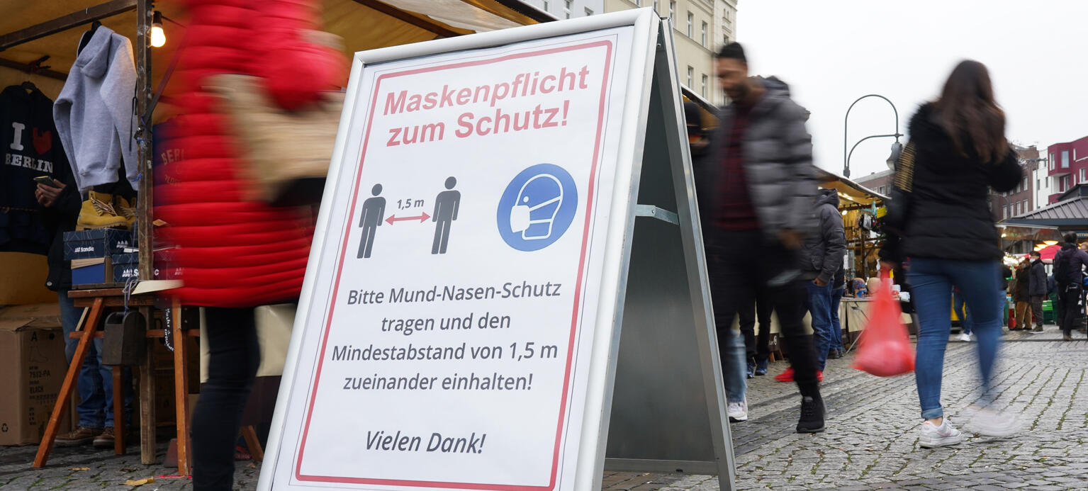 Ein Schild, das auf die Maskenpflicht und das Abstandsgebot hinweist, steht auf dem Wochenmarkt auf dem Hermannplatz