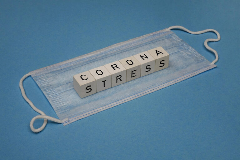 Auf einer Mundschutzmaske liegen Buchstabenwuerfel mit dem Wort Coronastress. PM zur Erwerbspersonenbefragung