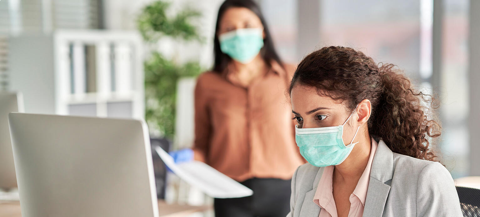 Young female professional wearing protective face mask working on computer at work place 