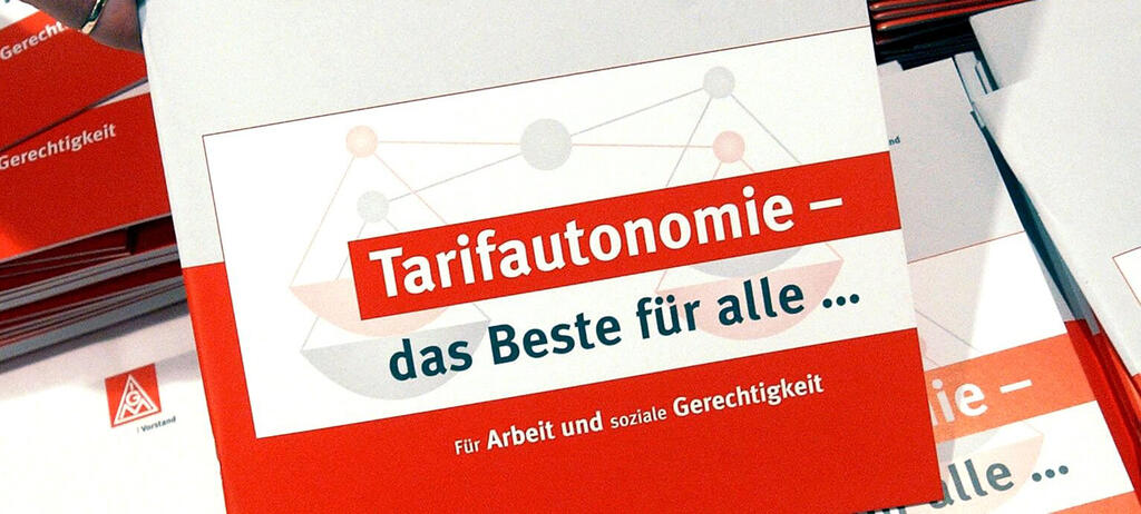Eine Hand greift nach einer Broschüre über Tarifautonomie .