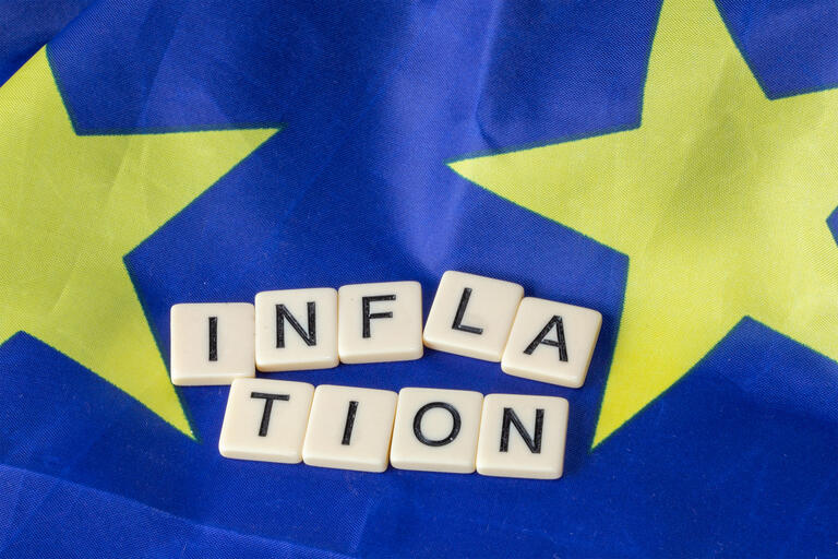 Symbolbild Inflation im Euroraum: Buchstabenwürfel zeigen das Wort Inflation auf einer Europaflagge an - Europäischer Tarifbericht