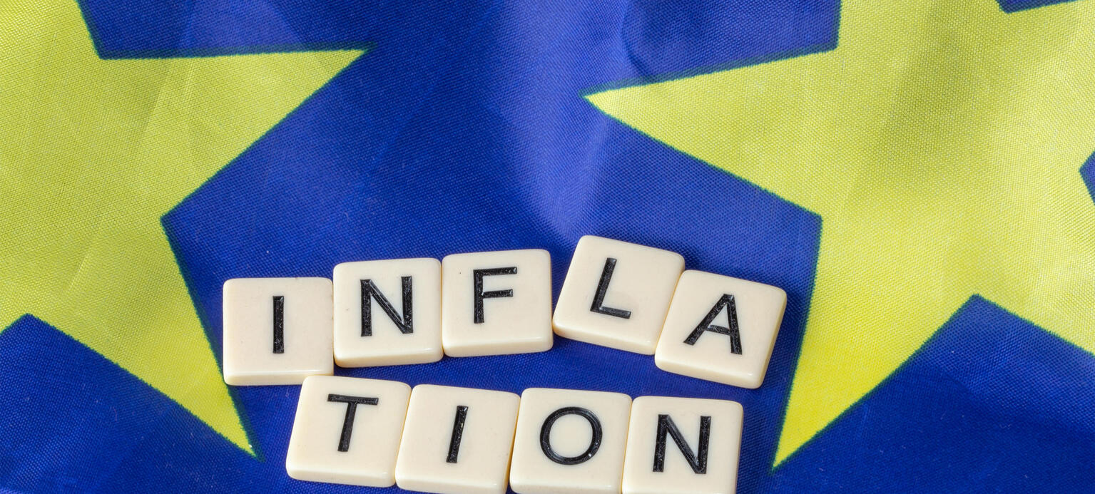 Symbolbild Inflation im Euroraum: Buchstabenwürfel zeigen das Wort Inflation auf einer Europaflagge an - Europäischer Tarifbericht