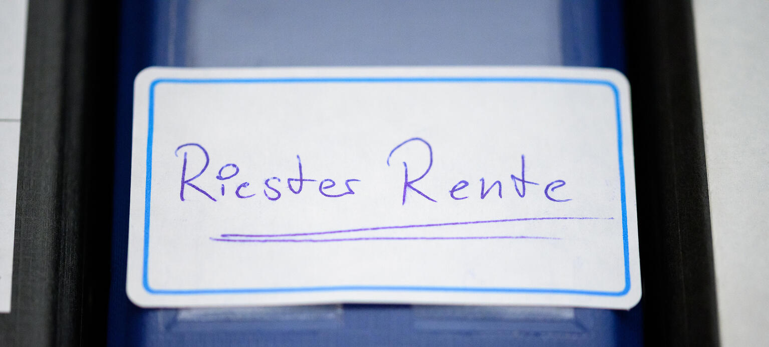 Ein Ordner mit einem Aufkleber 'Riester-Rente' steht in einem Regal.