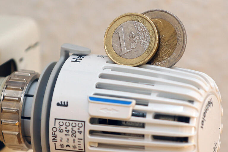 Auf einem Thermostat an einer Heizung liegen eine ein und eine zwei Euromünze