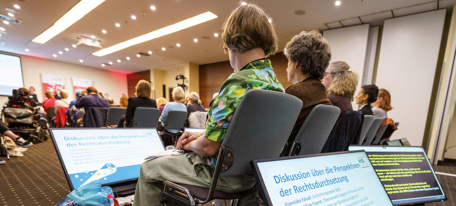 Bildschirme zwischen Stuhlreihen zum Mitlesen bei HSI-Veranstaltung zu Gleichstellung und Barrierefreiheit