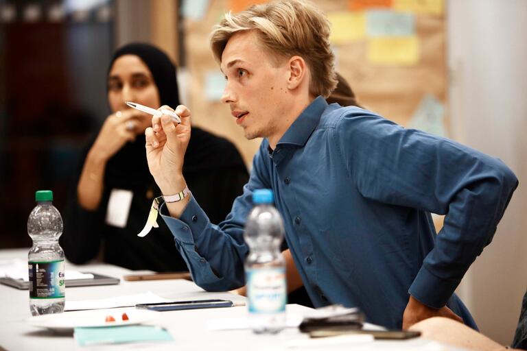 Teilnehmer der Sommerakademie beim Planspiel zu Tarifverhandlungen. Ein Teilnehmer redet und gestikuliert mit Stift in der Hand.