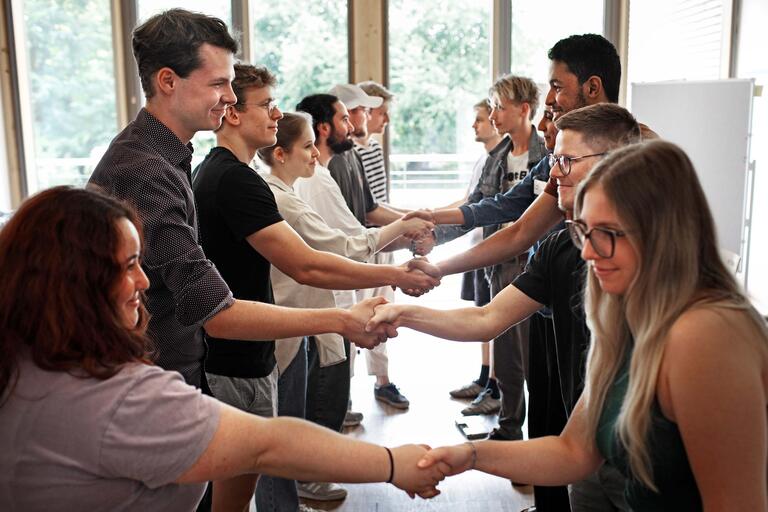 Teilnehmer des Planspiels zur Tarifverhandlungen schütteln sich im Stehen die Hände.