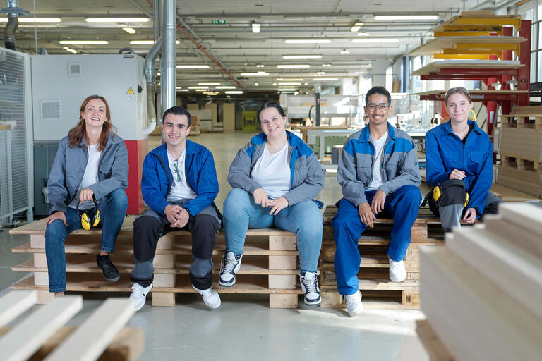 Fünf Auszubildende sitzen auf Europaletten und lächeln - Diversität