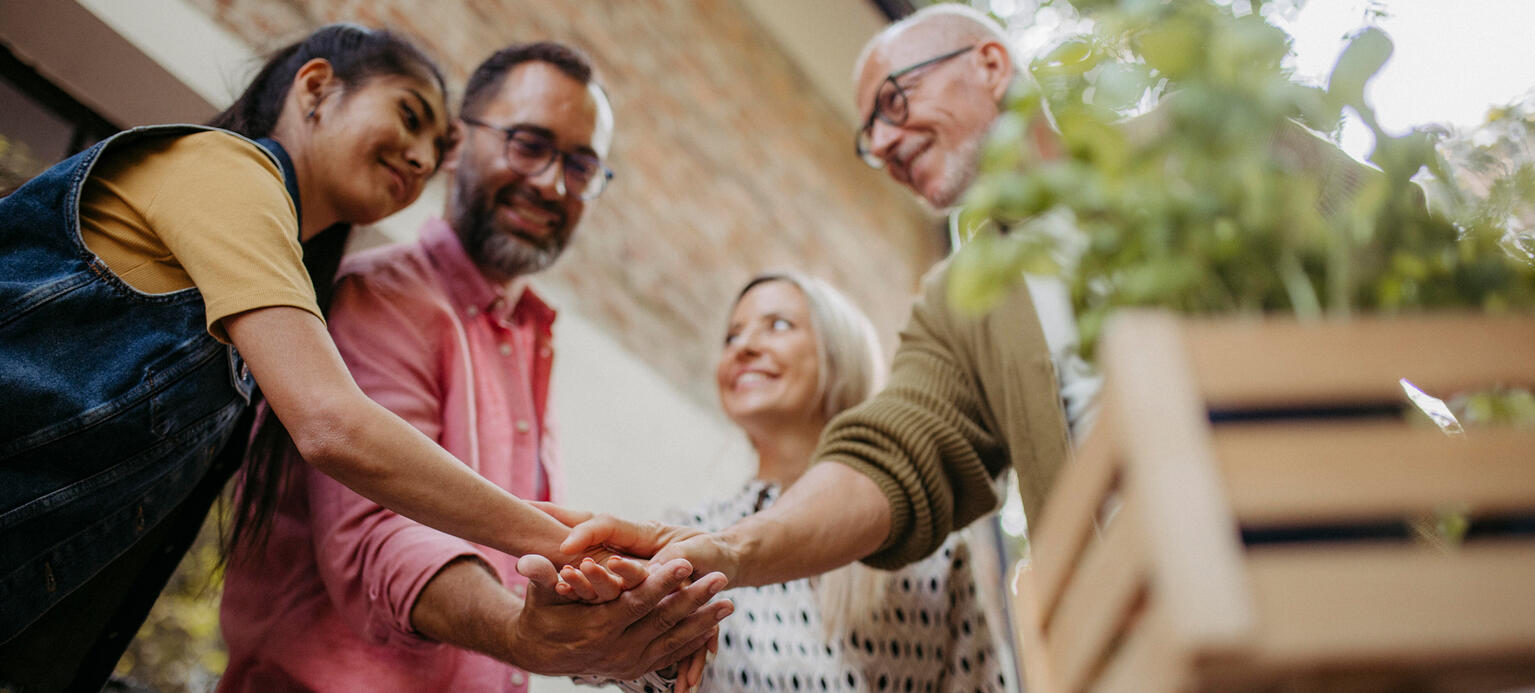 Symbolbild: Diverse Personen verschiedenen Alters und Herkunft stehen im Kreis und halten die Hände übereinander zusammen.