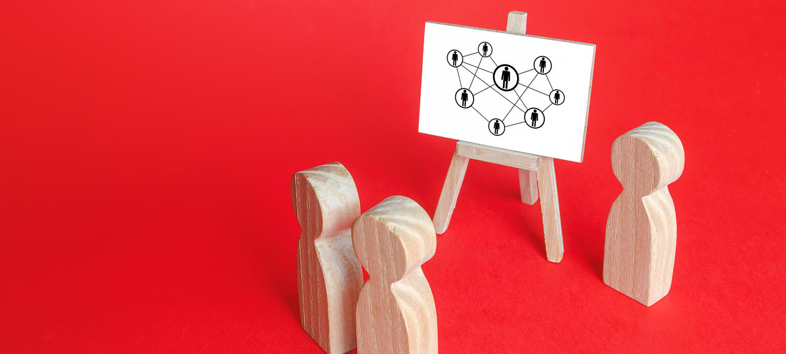 Symbolbild: Holzfiguren stehen vor einer Staffelei auf dem ein Chart steht. Auf dem Chart sind Verbindungen zwischen einzelnen Personen zu sehen.