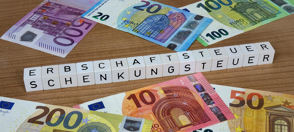 FOTOMONTAGE: Auf Geldscheinen befinden sich Buchstabenwuerfel mit den Schriftzuegen Erbschaftsteuer und Schenkungsteuer.