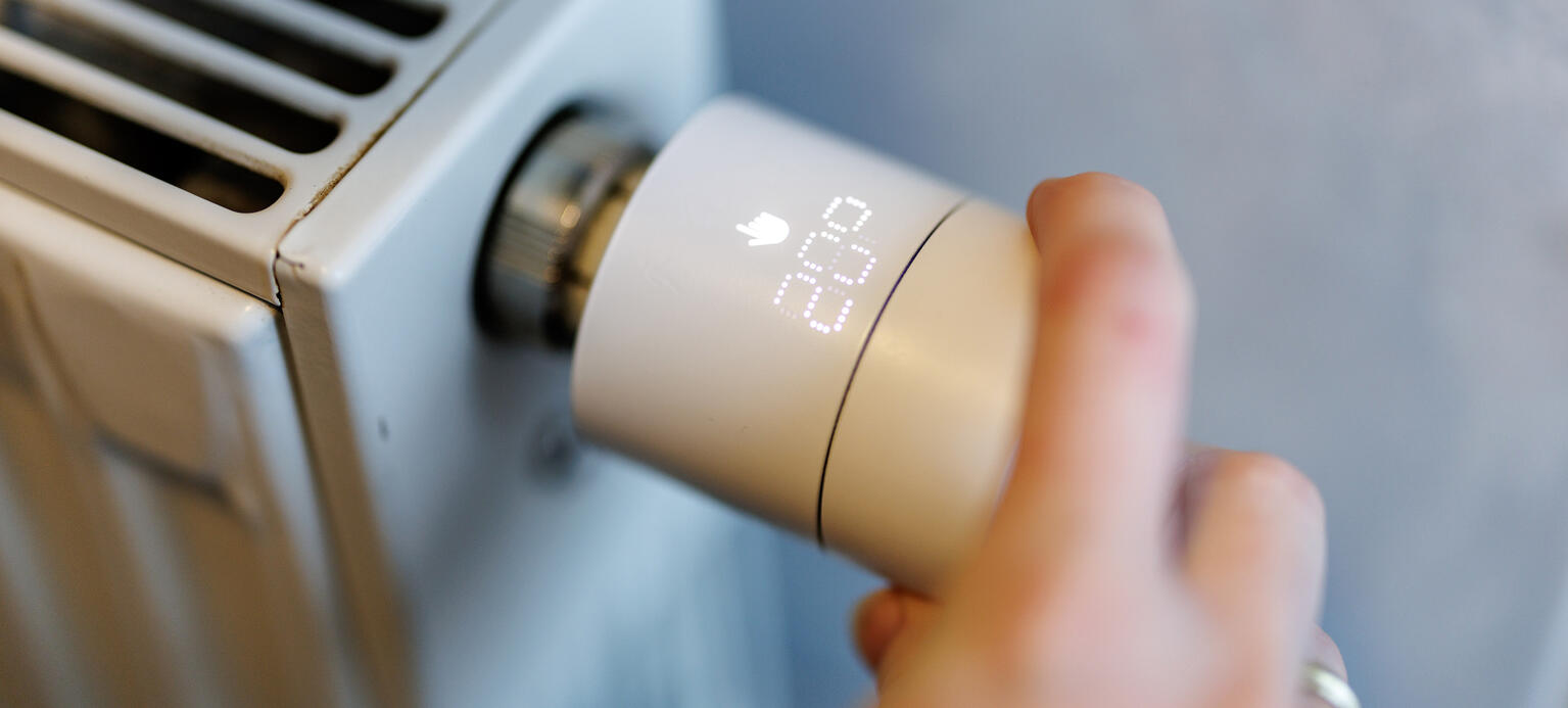 Eine Frau stellt an einem smarten Thermostaten die Temperatur von einem Heizkörper ein.