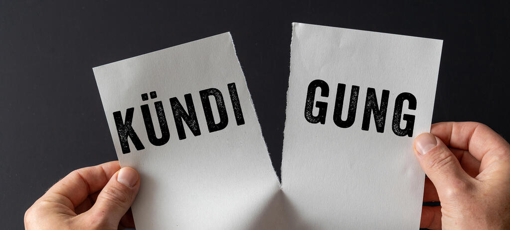 Zwei Hände halten ein zerrissenes Blatt Papier mit dem Wort Kündigung. Symbolbild Arbeitsplatzverlust, Entlassung und Ende eines Arbeitsverhältnisses