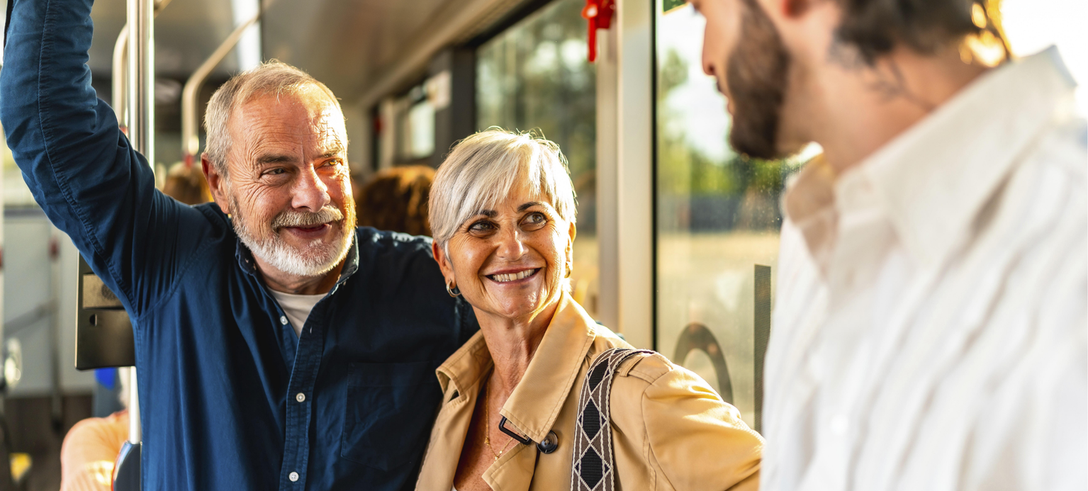 Glückliches Seniorenpaar plaudert mit einem jungen Mann, während es in einem modernen Stadtbus fährt, lächelt und genießt ihre Stadtreise, ihre soziale Verbindung und ihren entspannten Wochenendpendelverkehr