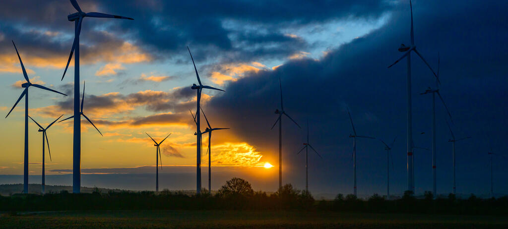 Der Sonnenaufgang leuchtet durch eine Wolkenlücke über einem Windenergiepark am frühen Morgen.