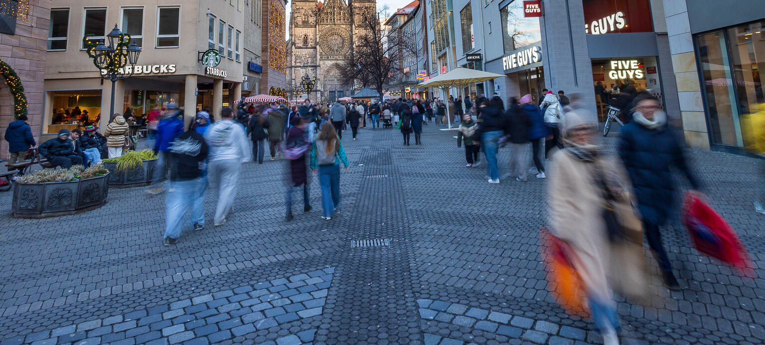 Das Bild zeigt ein urbanes Einkaufsumfeld mit vorweihnachtlicher Dekoration in der Fußgängerzone. 