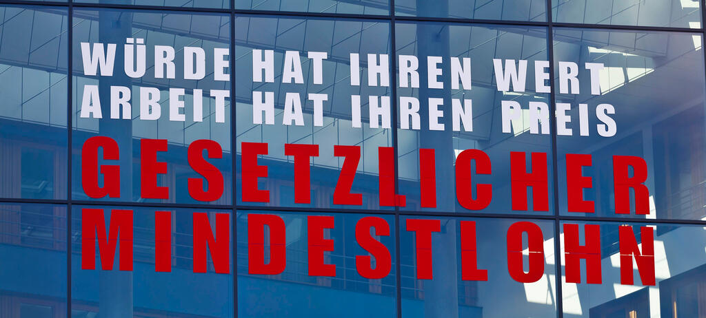 Auf Fensterscheiben eines Gebäudes steht geschrieben: 'Würde hat ihren wert, Arbeit hat ihren Preis! Gesetzlicher Mindestlohn!'