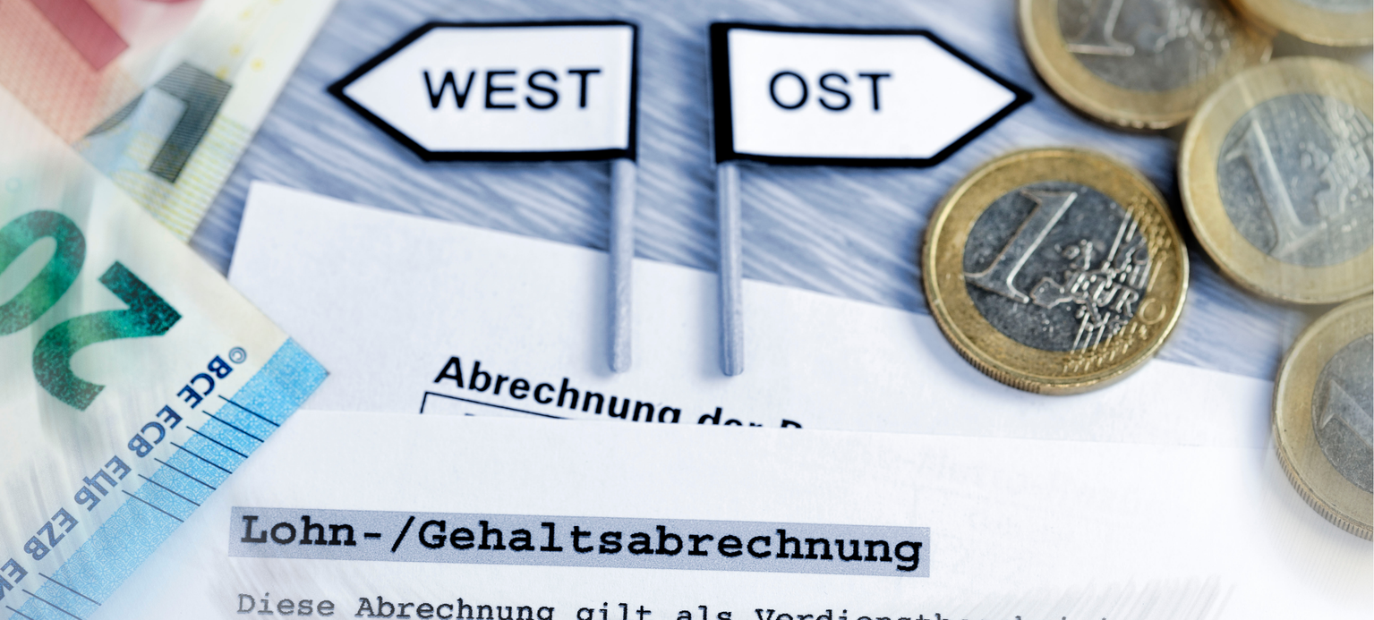 Wegweiser West und Ost mit Geldscheinen und Geldmuenzen, ungleiche Gehaelter in West- und Ostdeutschland